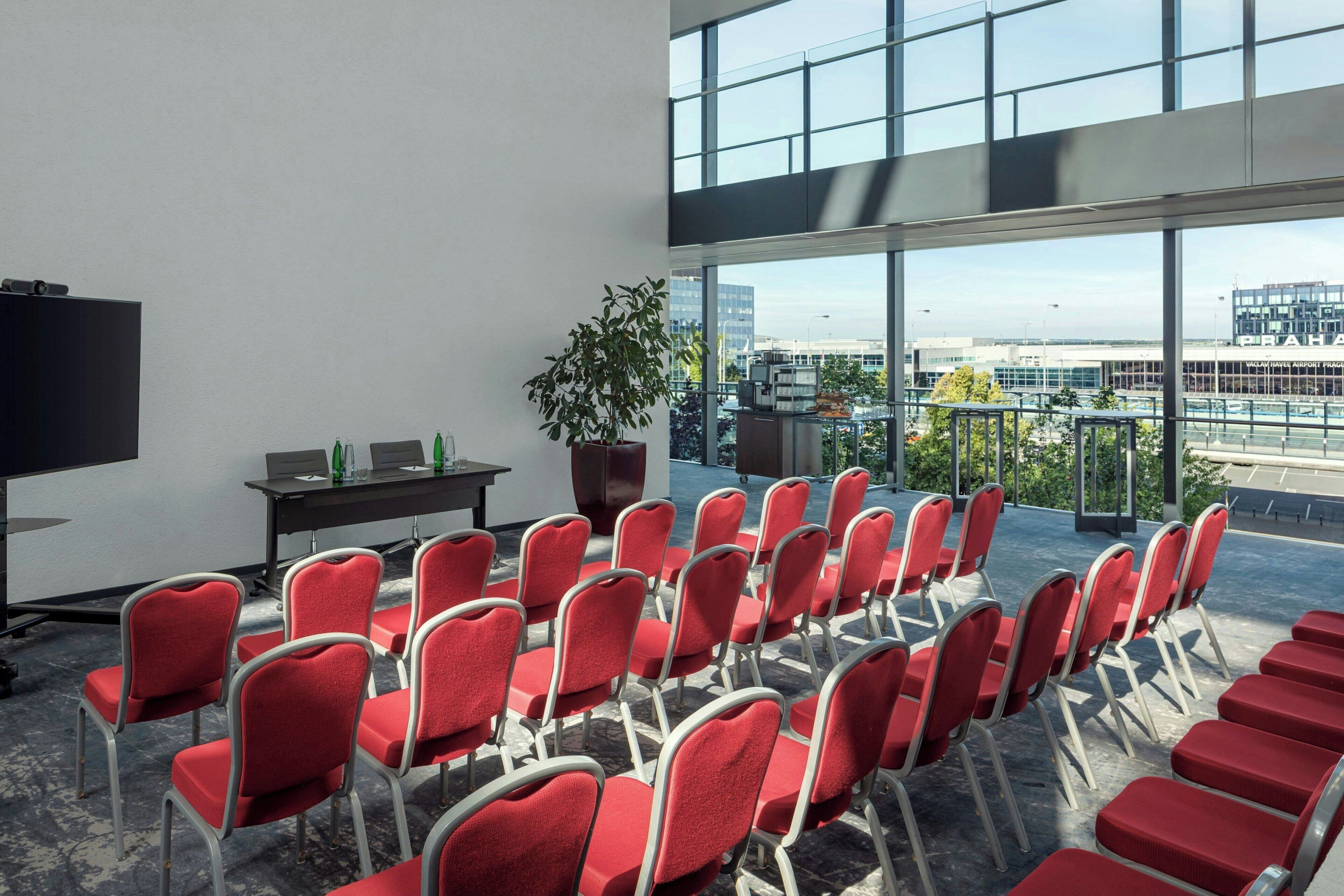 A conference room with red chairs, a large screen, a table with bottles, and a potted plant.