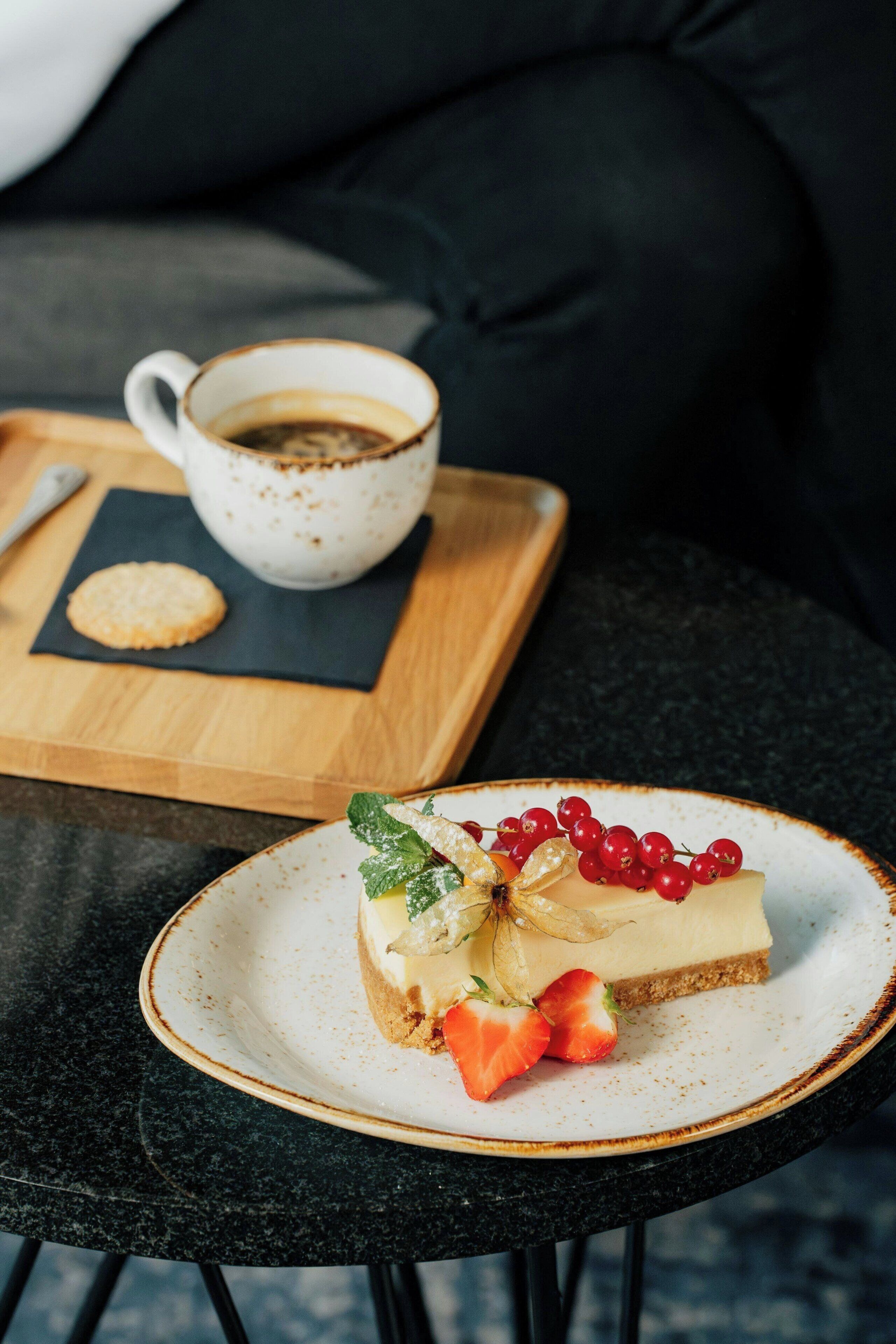 A dessert on a plate with a cup of coffee and a cookie on a wooden board.