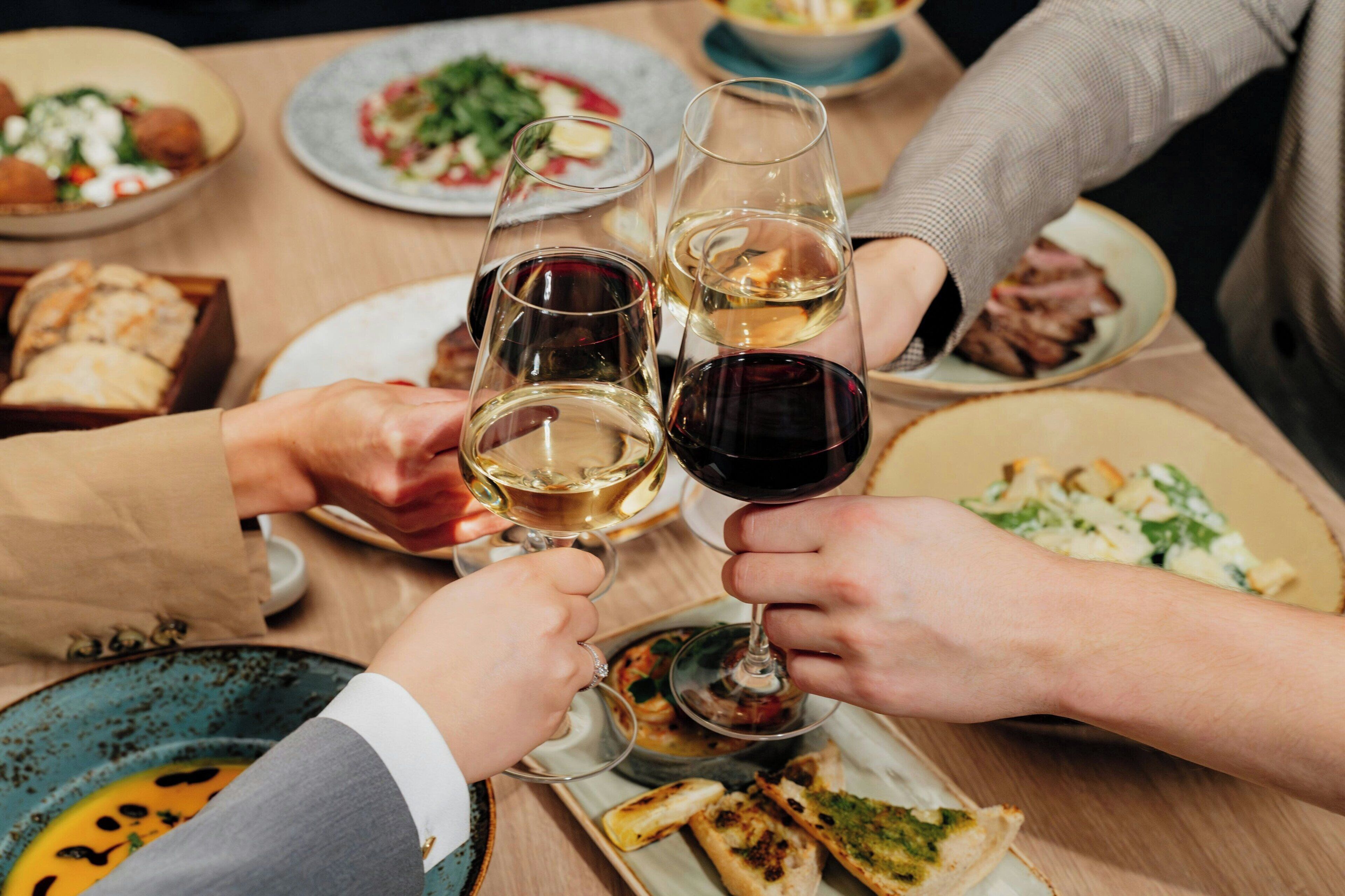 A group of people toasting with wine glasses at a dining table with various dishes.