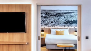 Une chambre d’hôtel moderne dotée d’un grand lit, d’un téléviseur à écran plat fixé au mur et offrant une vue sur la ville grâce à une grande fenêtre.