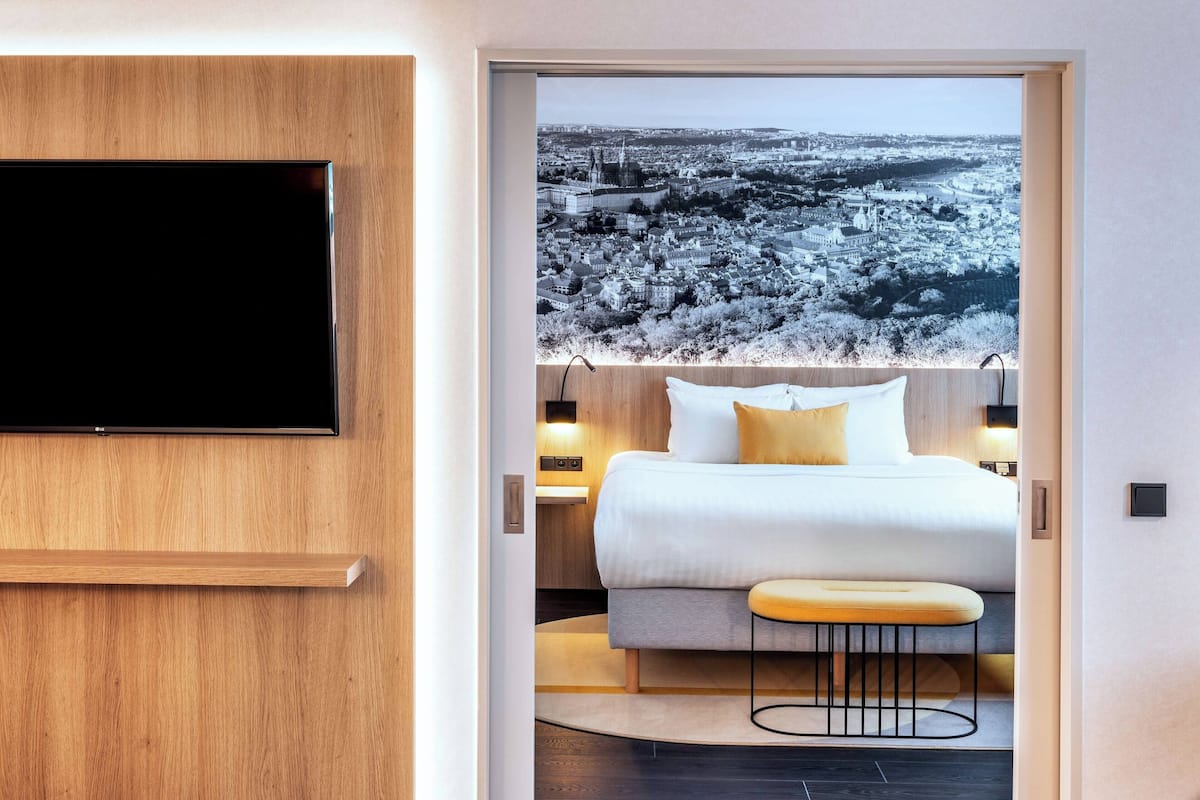 Een moderne hotelkamer met een groot bed, een flatscreen televisie aan de muur en een stadsgezicht door een groot raam.