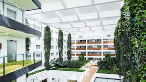 Un bâtiment moderne doté d’un atrium en verre, de plantes vertes et d’un intérieur à plusieurs niveaux.