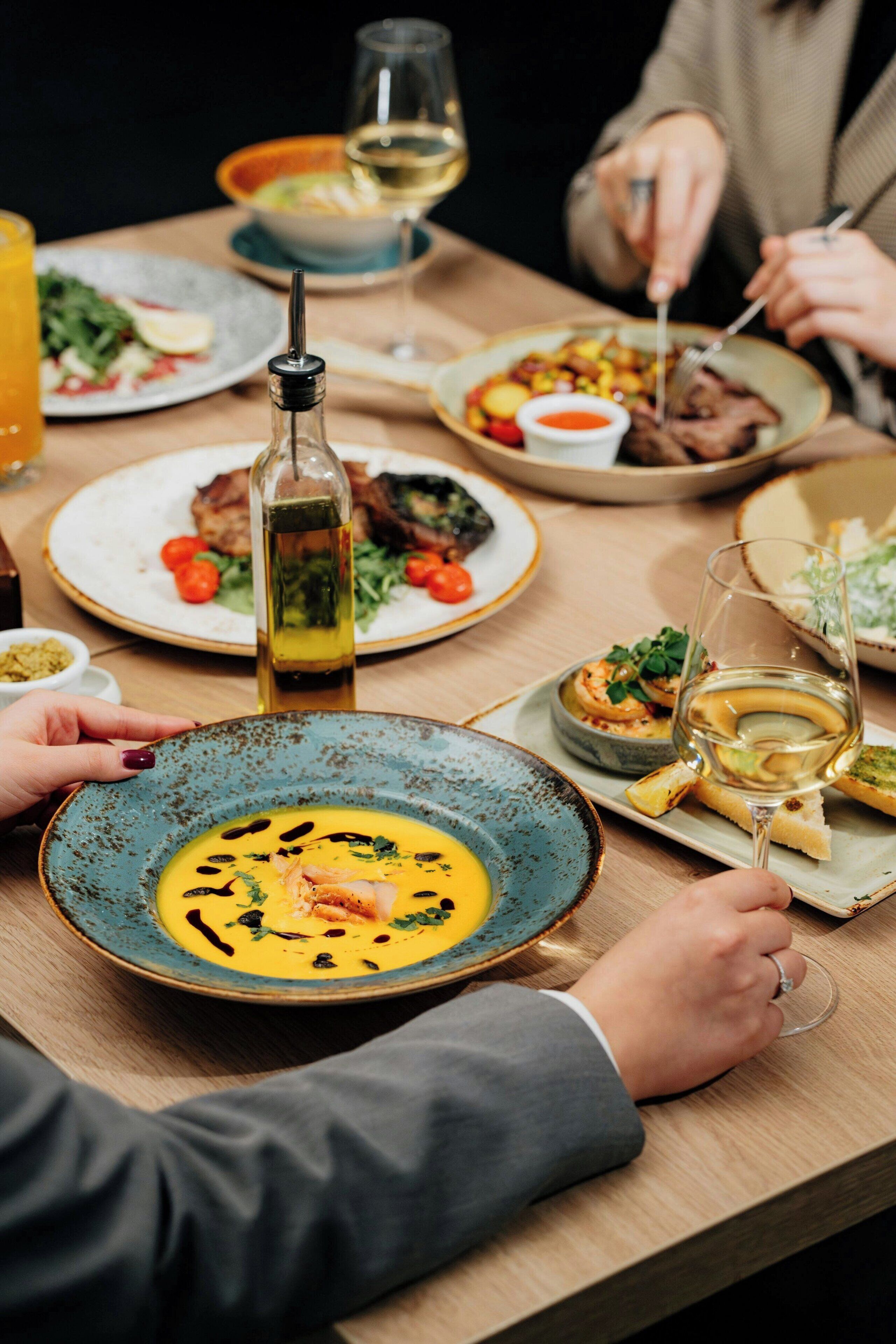 Una mesa de comedor con varios platos, una botella de aceite de oliva y copas de vino.