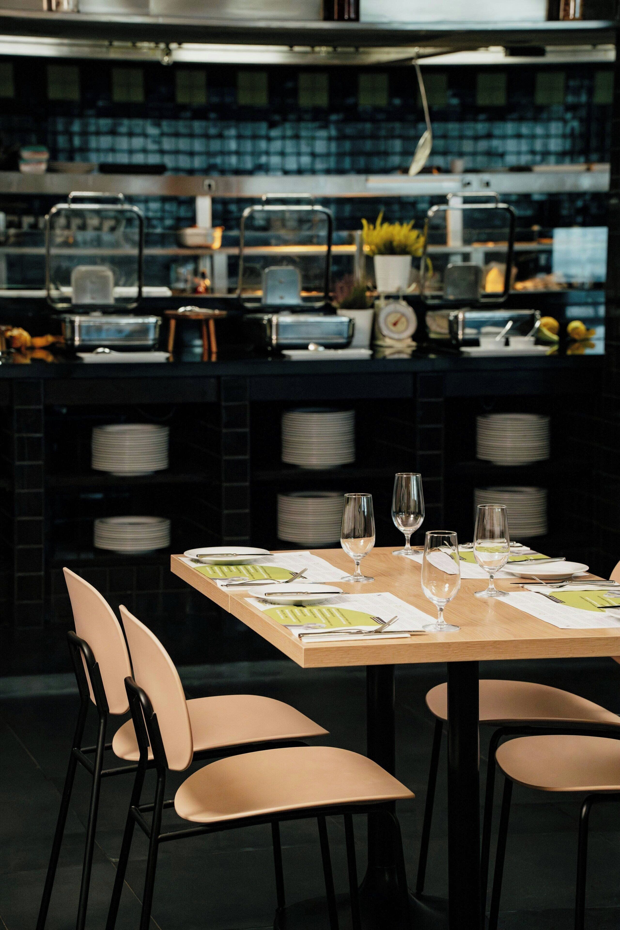 A restaurant with a wooden table set for dining, chairs, and a kitchen area in the background.
