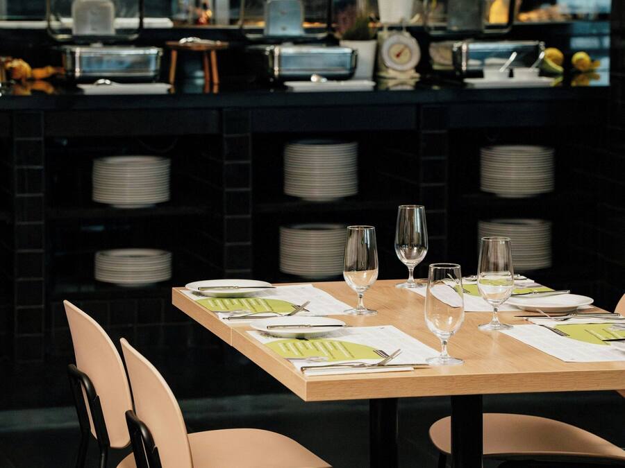 Un restaurante con una mesa de madera dispuesta para comer, sillas y una zona de cocina al fondo.