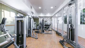 A gym with various exercise machines, a mirrored wall, and a view of palm trees through the windows.