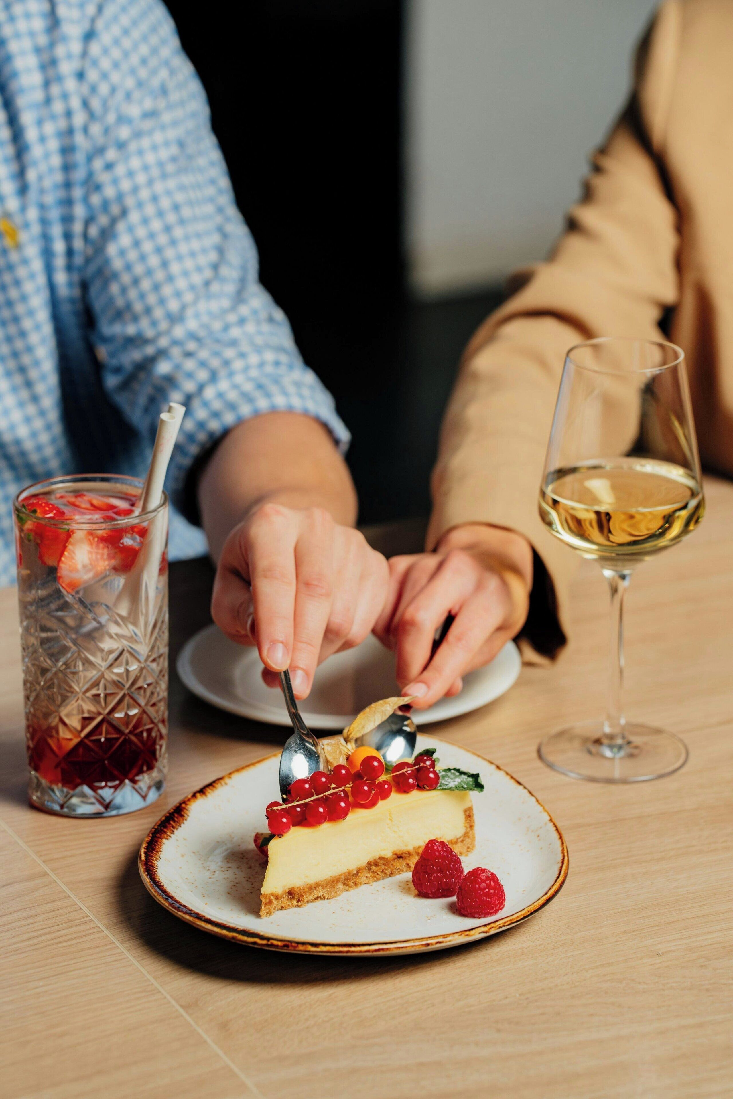 A dessert plate with a slice of cheesecake, strawberries, and red currants on a ceramic plate.