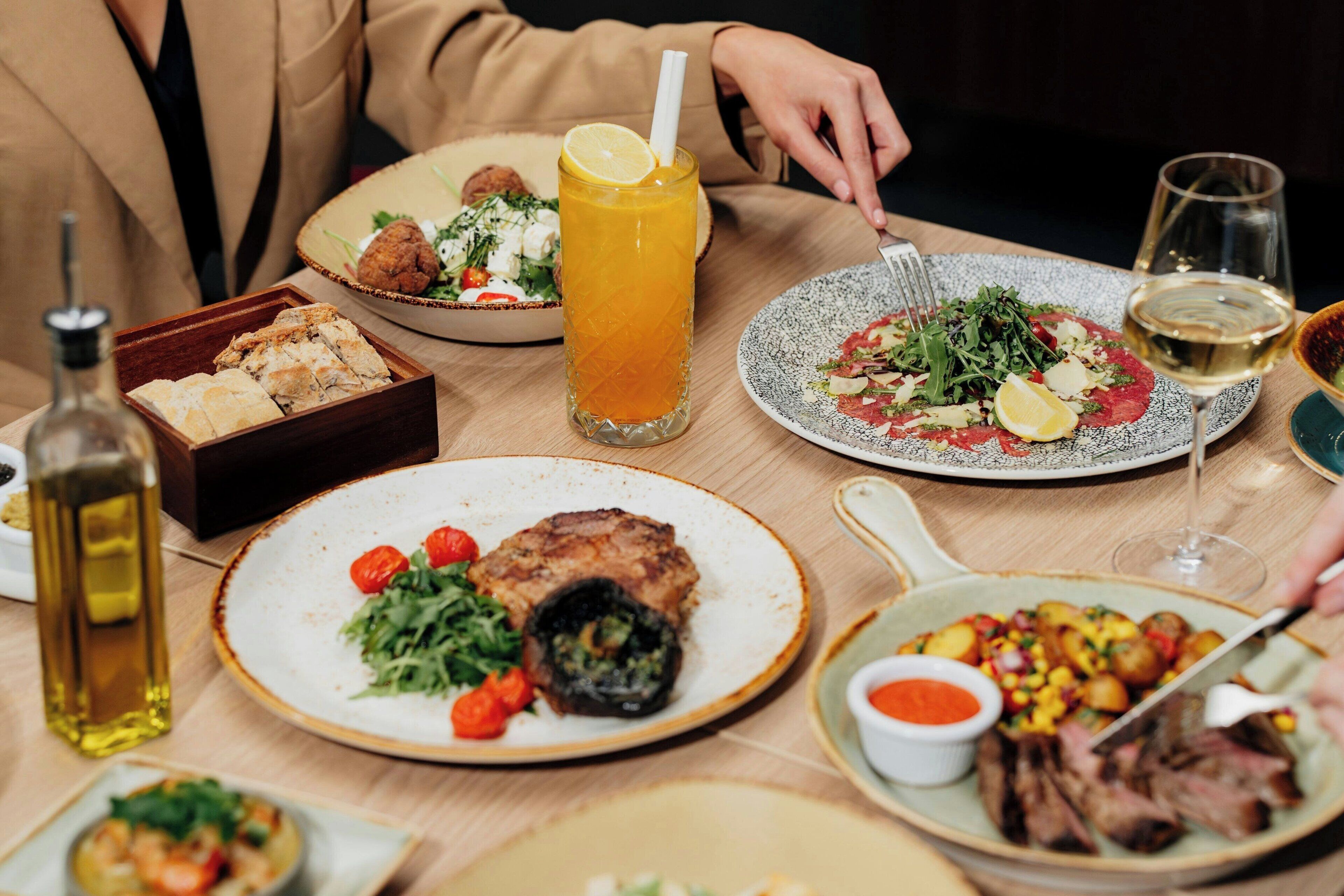 Une table à manger avec différents plats, un verre de jus d’orange et une bouteille d’huile d’olive.