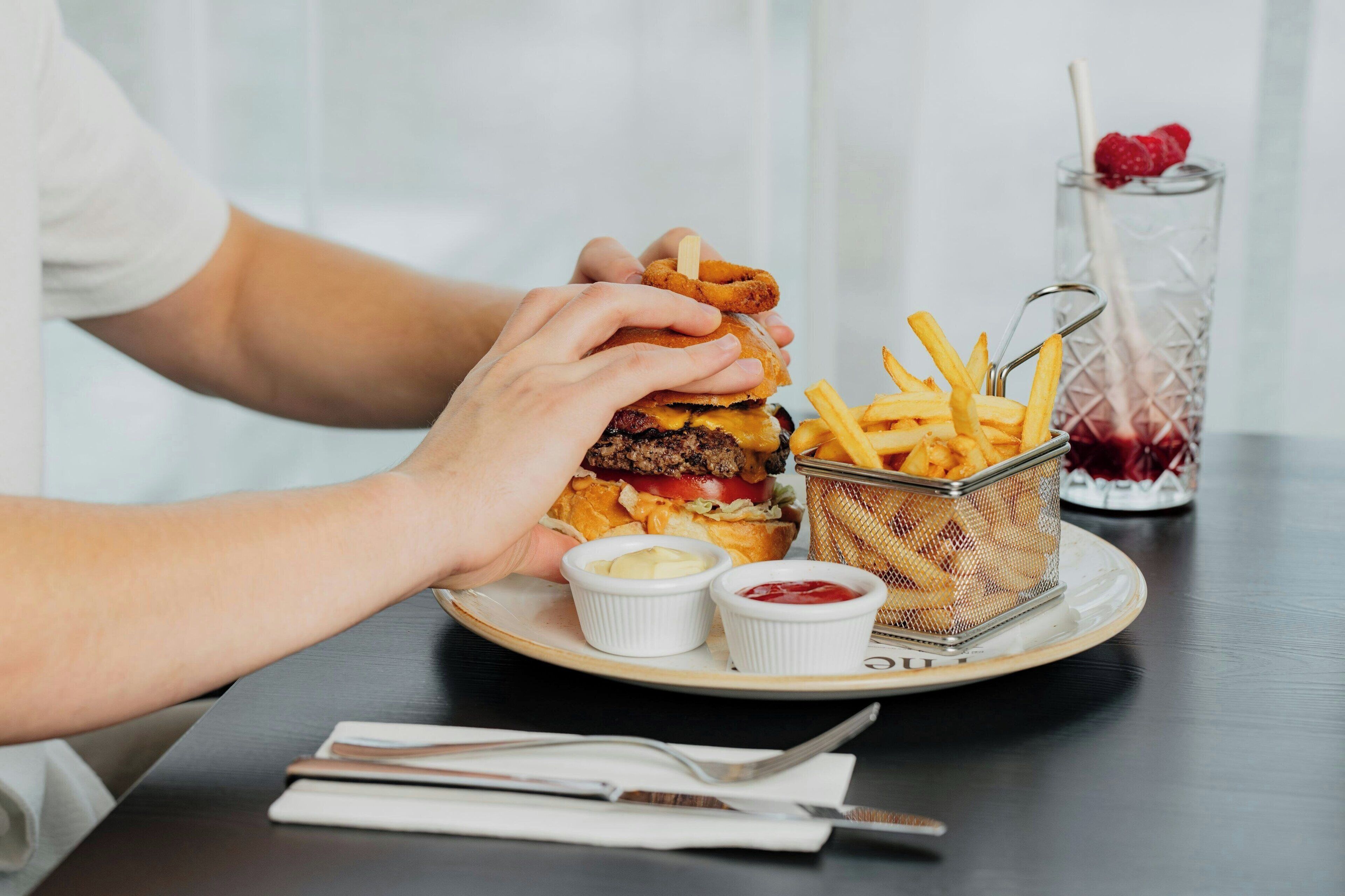A plate with a burger, fries, and two small containers of condiments.