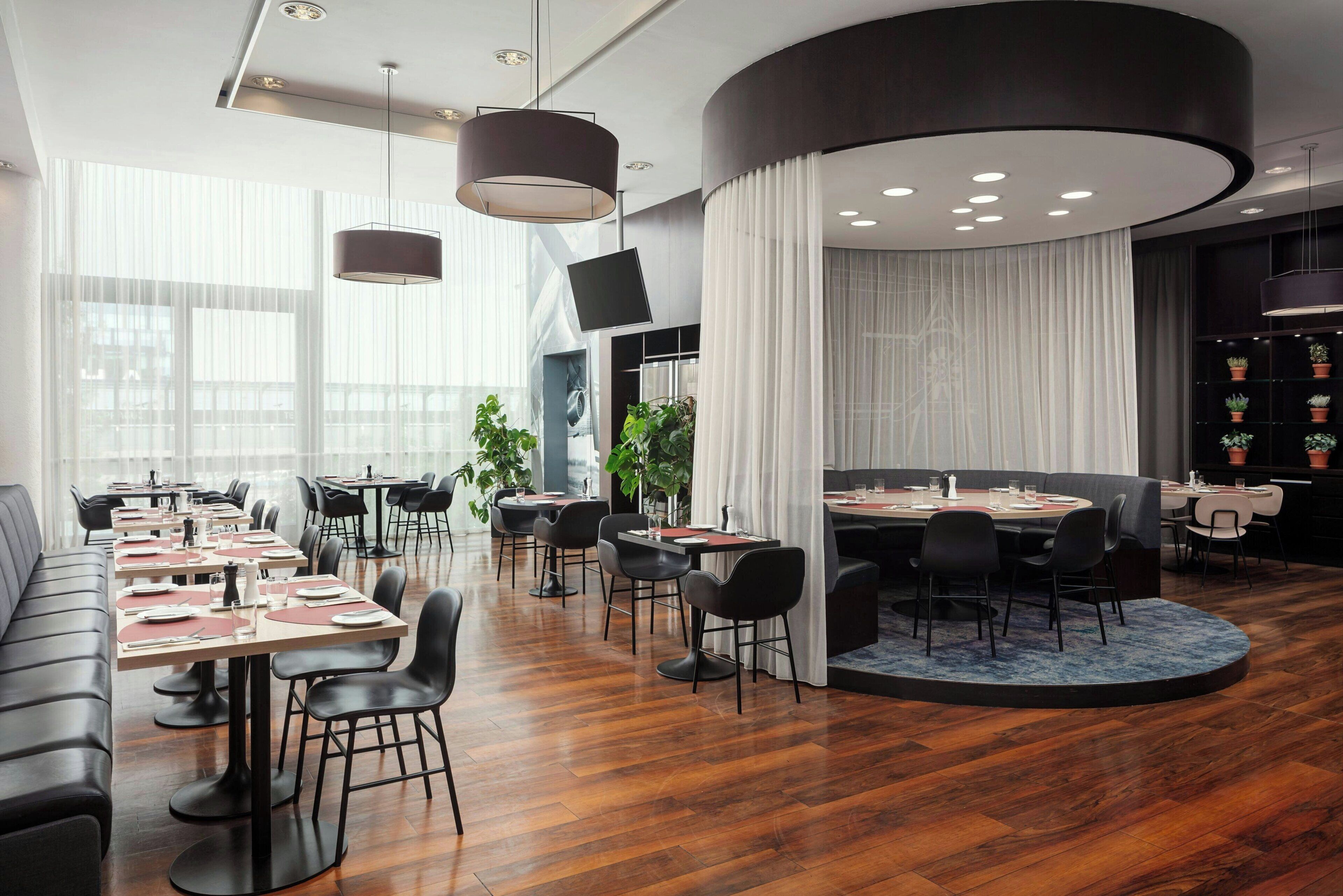 A modern dining area with multiple tables, black chairs, and a large round table.