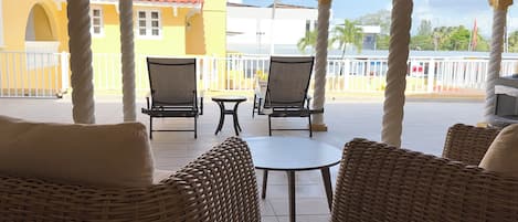 Un espacio de estar al aire libre cubierto con mobiliario de mimbre y vistas a edificios al fondo.
