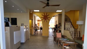 A hotel lobby with a reception desk, a staircase, and a seating area with a sun mural. - Hotel Villa del Sol (Carolina)