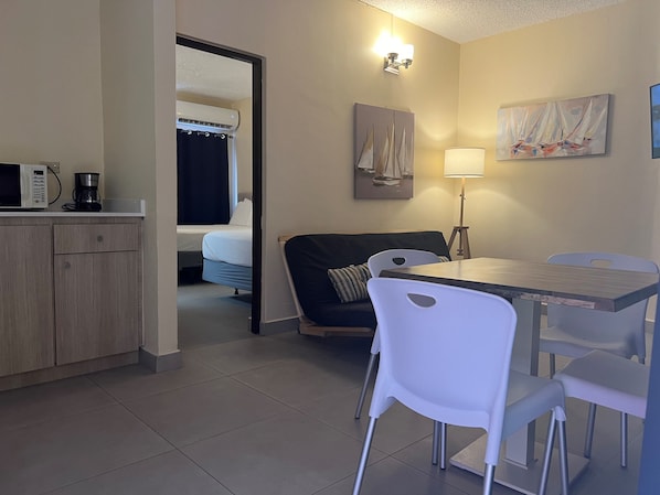 Une chambre d’hôtel compacte comprenant un coin cuisine, un lit, un espace repas et un petit salon.