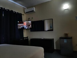 Habitación de hotel con cama, escritorio, espejo, equipo de aire acondicionado y un pequeño cubo de basura.