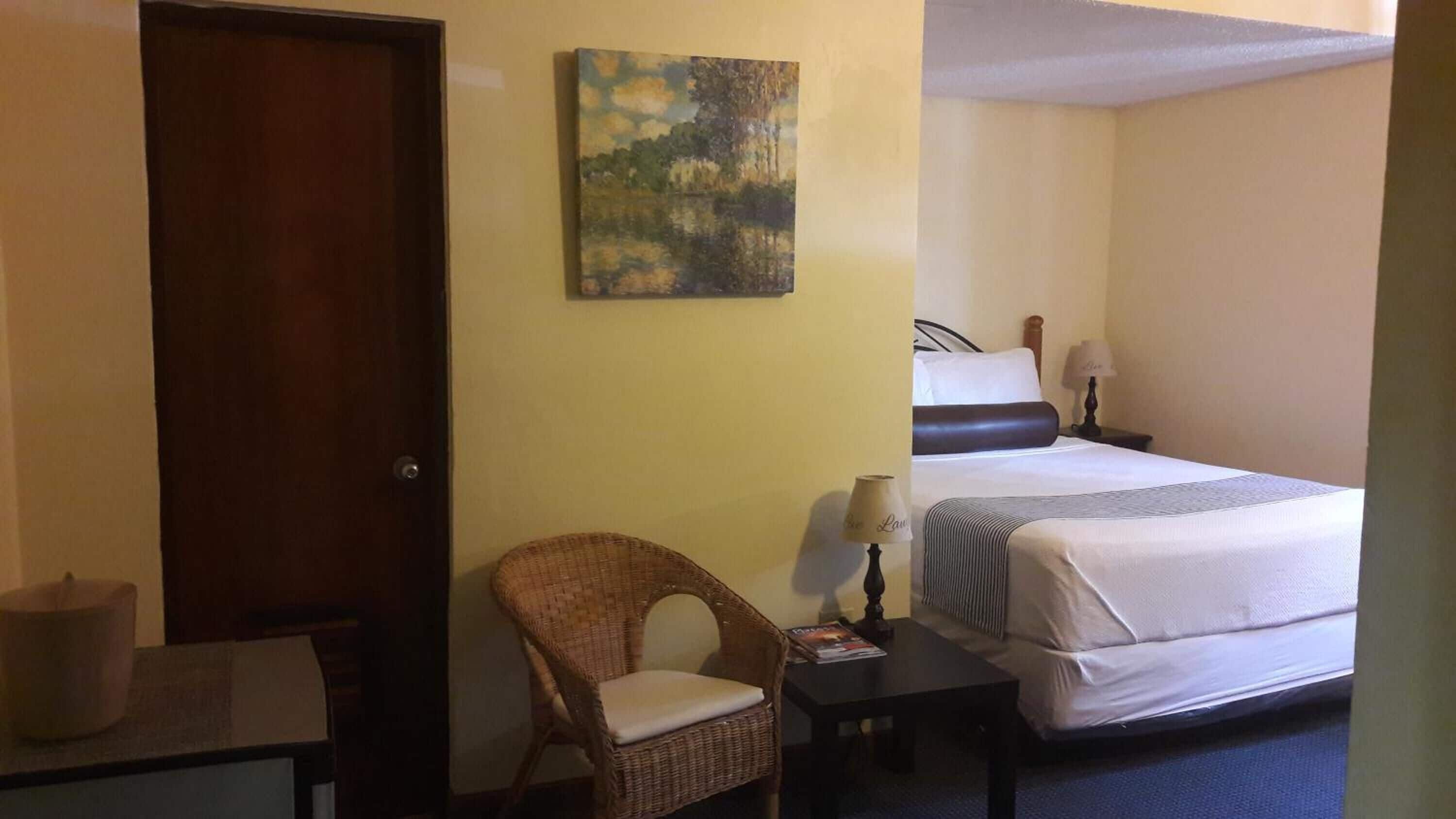 Une chambre d’hôtel avec un lit, une chaise, une petite table, une lampe et un tableau au mur.