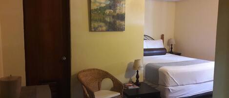 Een hotelkamer met een bed, een stoel, een klein tafeltje, een lamp en een schilderij aan de muur.