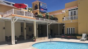 A hotel with a pool, outdoor seating, and a covered area with a red umbrella. - Hotel Villa del Sol (Carolina)
