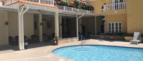 Un hotel con piscina, mobiliario exterior y una zona cubierta con un paraguas rojo.