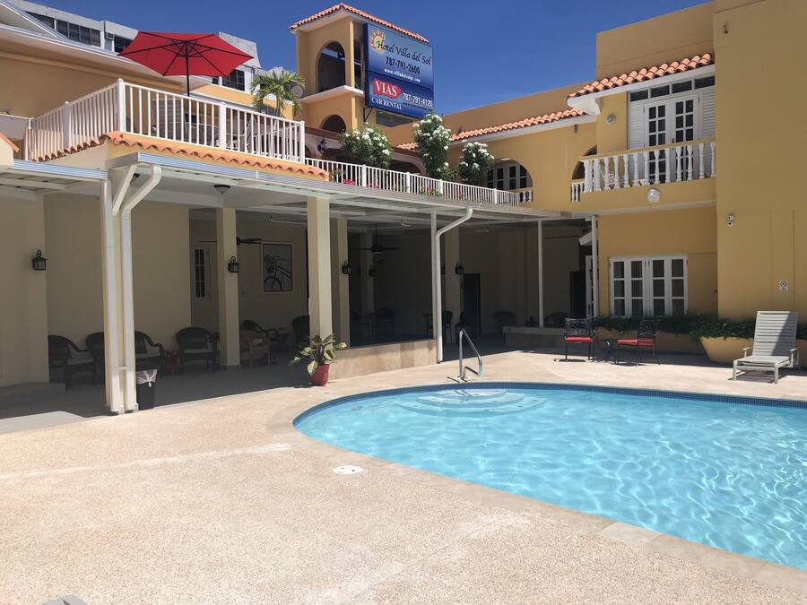 A hotel with a pool, outdoor seating, and a covered area with a red umbrella.