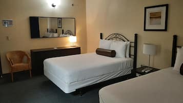 Una habitación de hotel con una cama, una silla, un escritorio con lámpara, una mesita de noche con lámpara, un cuadro en la pared y una luz en el techo.