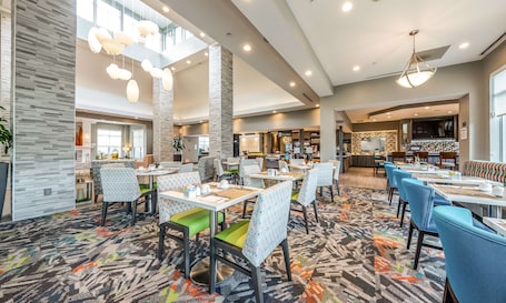 A spacious hotel lobby with multiple dining areas, a central bar, and a visible shop.