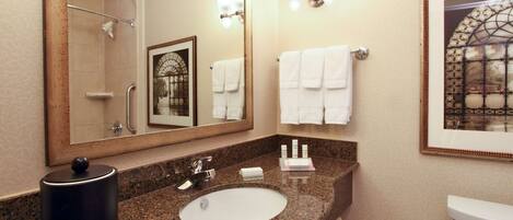 A bathroom with a granite countertop, a sink, a toilet, a shower, and a large mirror.