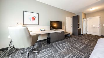 A hotel room with a desk, chair, television, and two doors.