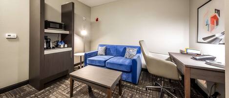A hotel room with a blue sofa, a desk with a computer, a coffee maker, and a microwave.