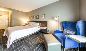 Ein Hotelzimmer mit Bett, Nachttisch, Lampe, Stuhl und einem Kunstwerk an der Wand.
