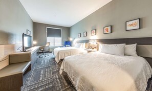 A hotel room with two beds, a desk, a chair, a TV, and artwork on the walls.