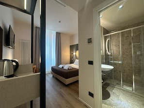 A modern hotel room with a bed, bedside table, and a glass-enclosed shower area. - Hotel Porta Pia (Rome)