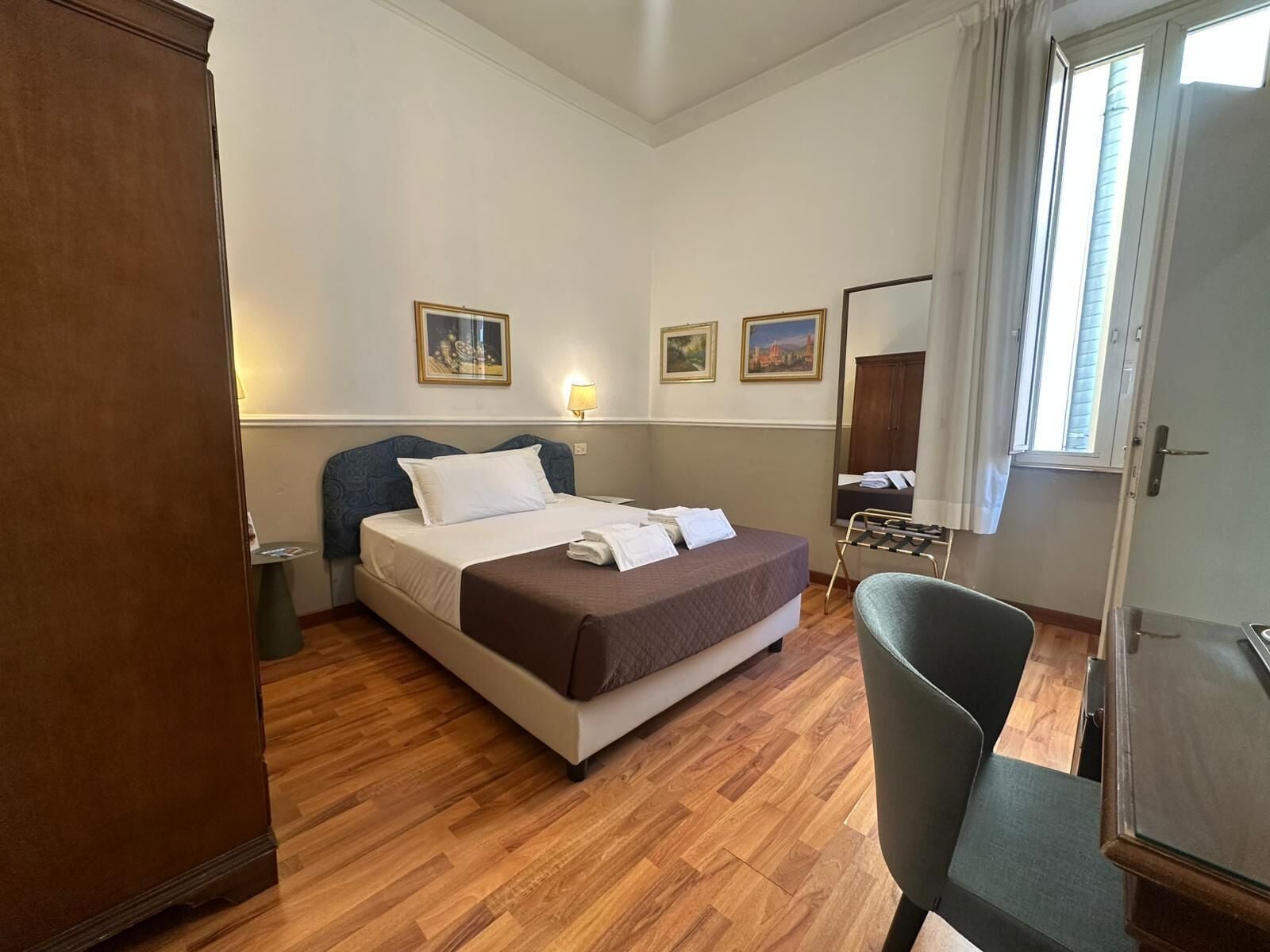 A hotel room with a bed, a chair, a desk, and a window.