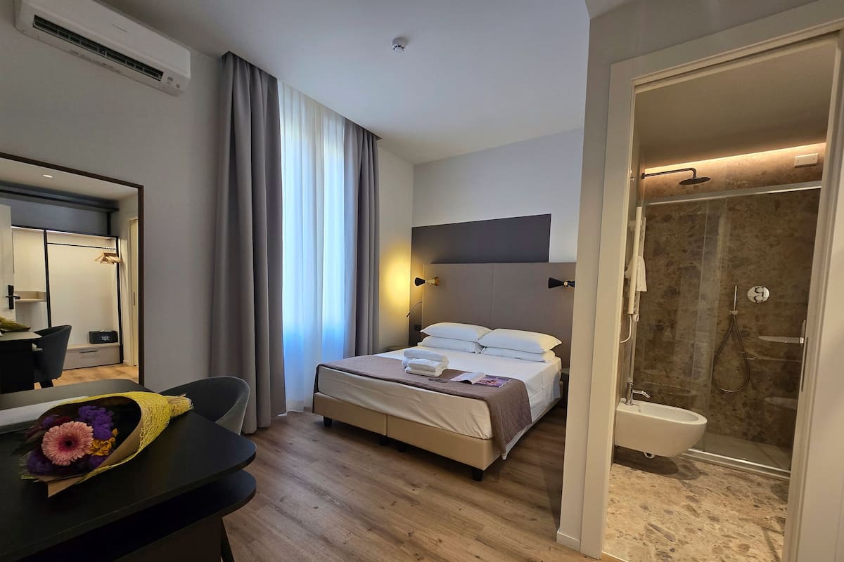 A hotel room with a bed, bedside table, and a shower area.