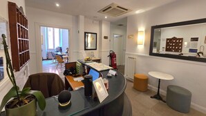 A hotel reception area with a reception desk, a fire extinguisher, a mirror, and a seating area in the background. - Hotel Porta Pia (Rome)