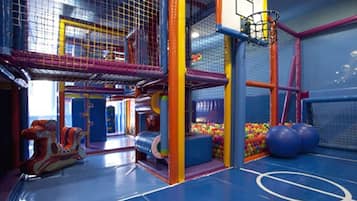 Un área de juegos interior con canasta de baloncesto, estructuras de juego coloridas y una piscina de pelotas.