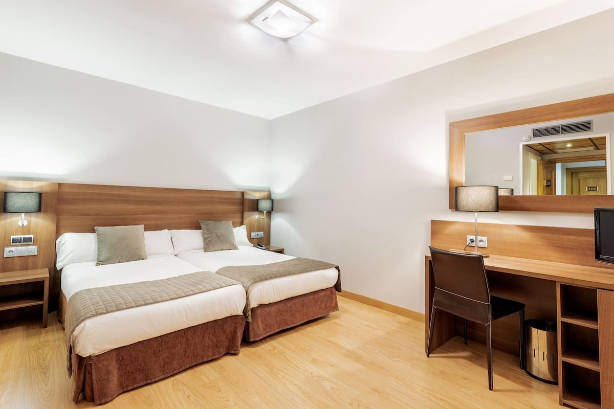 Una habitación de hotel con dos camas, un escritorio y un espejo.