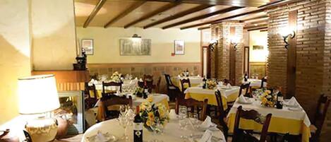 A restaurant with round tables set for dining, wooden beams on the ceiling, and brick walls.