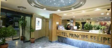 Zona de recepción de hotel con suelo de mármol, un tragaluz circular grande y un mostrador de recepción con la leyenda 'HOTEL PRINCIPE FELIPE'.