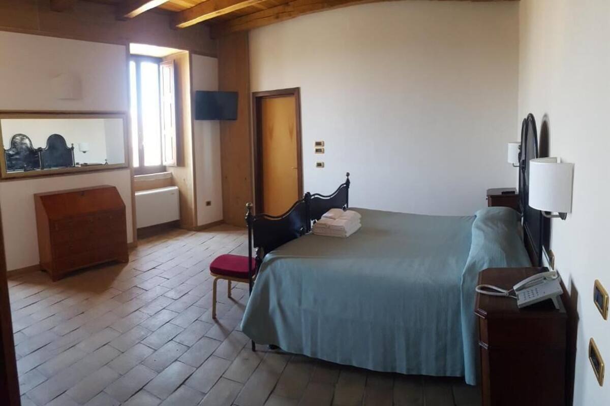A bedroom with a bed, a chair, a dresser, a mirror, and a bedside table with a phone.