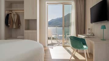 Habitación de hotel con cama, escritorio con silla, televisor y vista a la montaña y al agua a través de una puerta corredera.