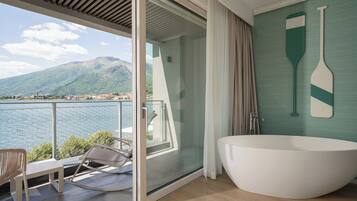 Un balcón con vista a un lago y montañas, una bañera blanca y una silla.