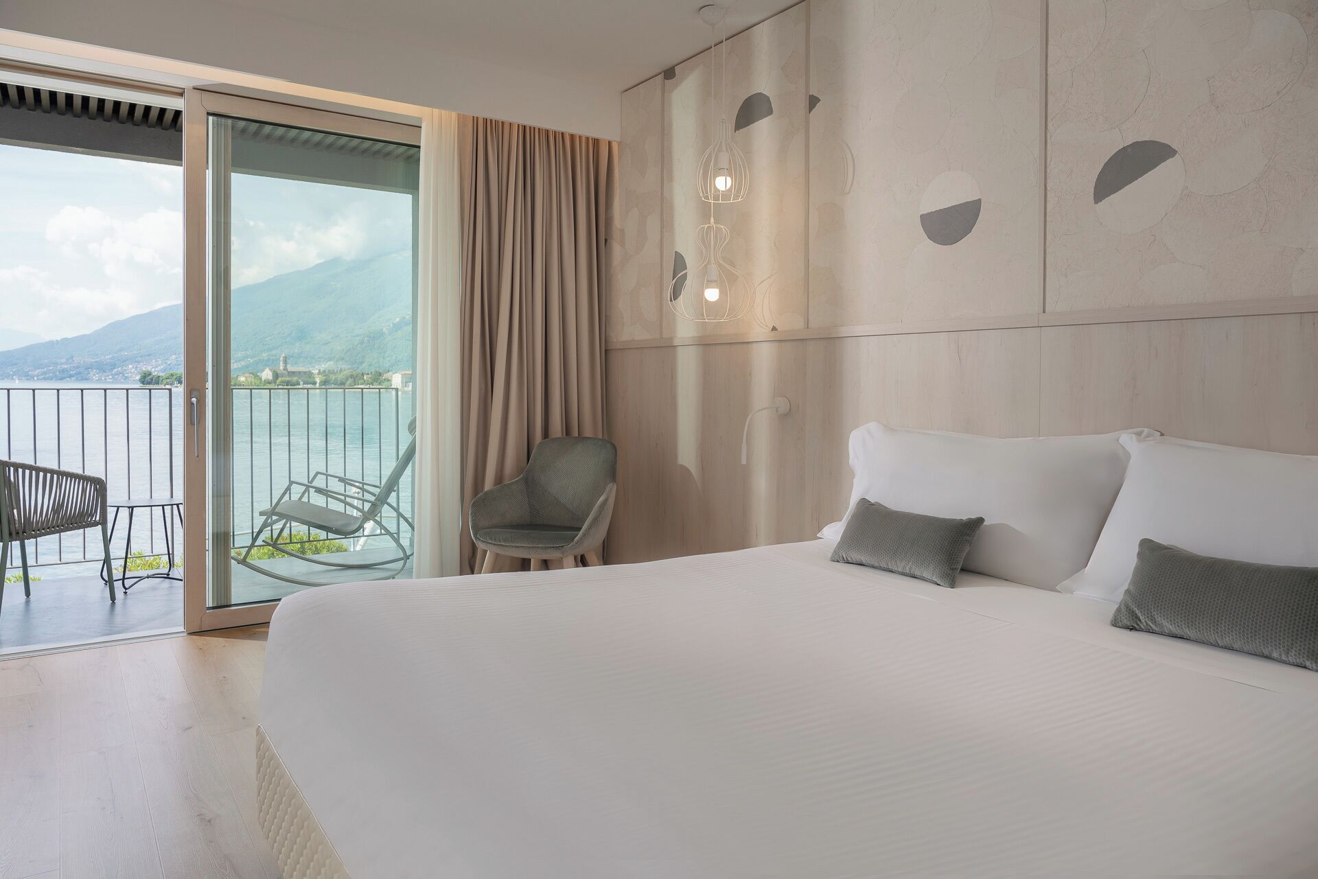 Ein Hotelzimmer mit einem großen Bett, einem Sessel, einem Balkon mit Bergblick und einer modernen Leuchte.