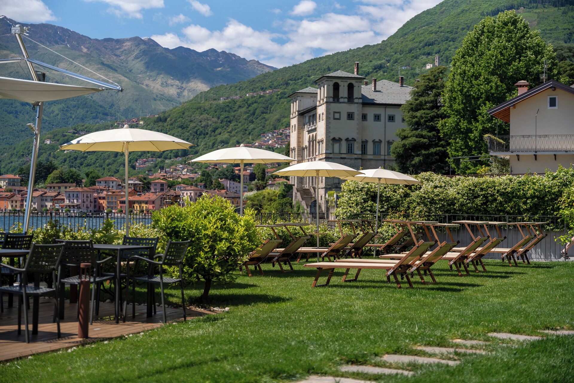 Eine Terrasse mit Sitzgelegenheiten im Freien, Sonnenschirmen und Blick auf einen See und Berge.