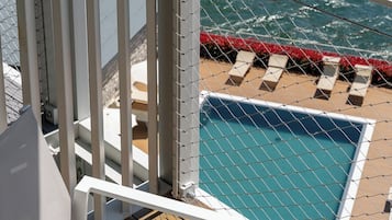 A pool area with a view of the ocean, deck chairs, and a white railing.