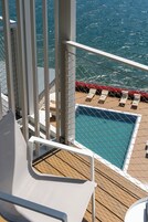 Zona de piscina con vista al océano, sillas de sol y barandilla blanca.