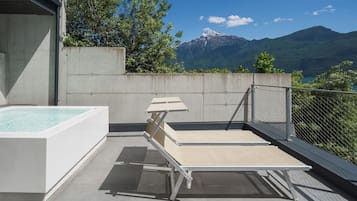 A rooftop terrace with a hot tub, lounge chairs, and a view of mountains.