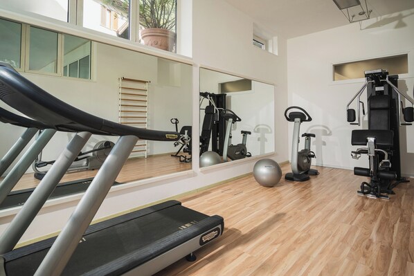 A gym with a treadmill, exercise bikes, and a mirror reflecting the equipment. - Hotel Regina (Gravedona)