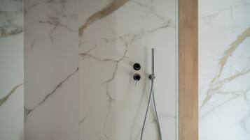 A bathroom with a marble wall, a shower with a handheld showerhead, and a wooden frame.