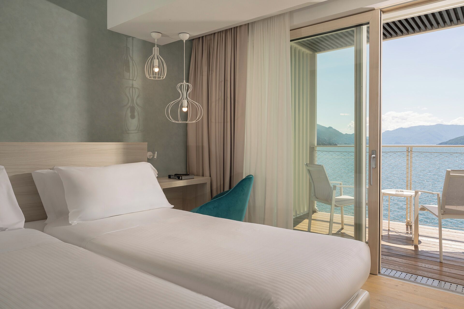 Ett hotellrum med en stor säng, ett skrivbord, en stol och en balkong med utsikt över havet.