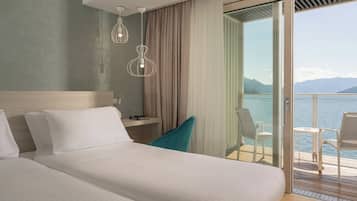 Ett hotellrum med en stor säng, ett skrivbord, en stol och en balkong med utsikt över havet.